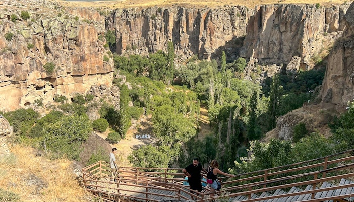 Visitors descending wooden stairs into Ihlara Valley, Cappadocia, surrounded by cliffs and greenery.