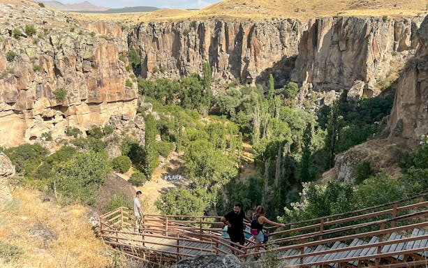 Visitors descending wooden stairs into Ihlara Valley, Cappadocia, surrounded by cliffs and greenery.