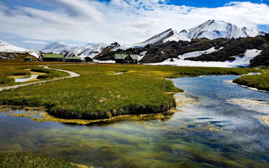 Landmannalaugar landscape with snowy mountains, green fields, and a winding stream in Iceland.