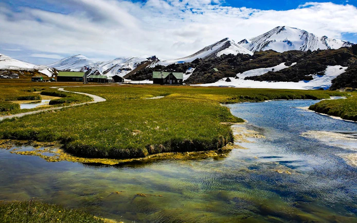 Landmannalaugar landscape with snowy mountains, green fields, and a winding stream in Iceland.