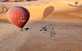 Hot air balloon preparing for flight over Wadi Rum desert with vehicles below.