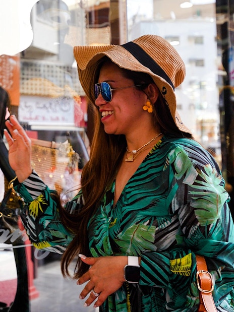 Woman admiring large gold jewelry display in Dubai shop window.