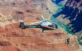 Helicopter flying over Grand Canyon South Rim with river view.