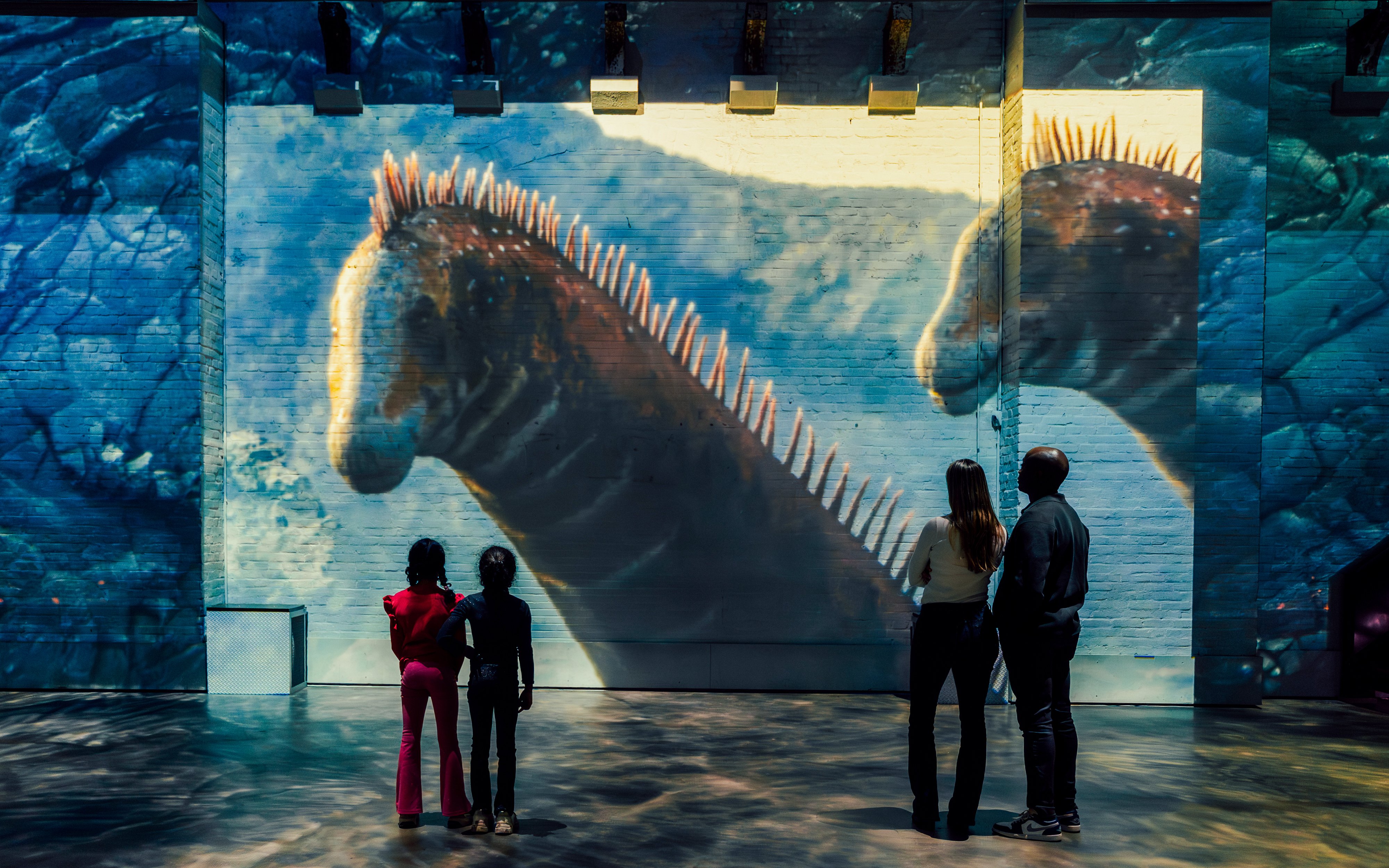 Visitors viewing large dinosaur projections at Prehistoric Planet: Dinosaurs – The Immersive Experience.