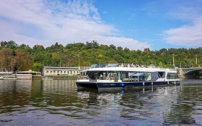 Cruise boat on Vltava River with passengers enjoying scenic views of Prague.