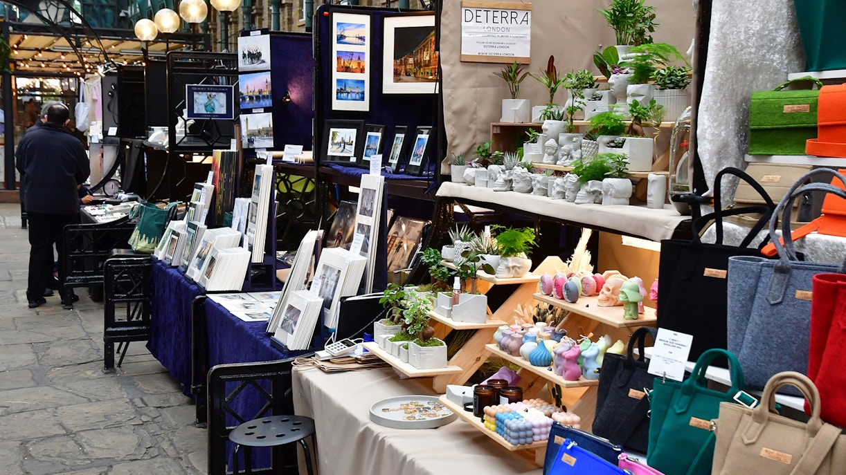 Market stalls with art, plants, and bags in Covent Garden district, London.