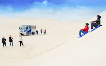 People sandboarding on dunes with a 4WD vehicle in Lancelin, Australia.