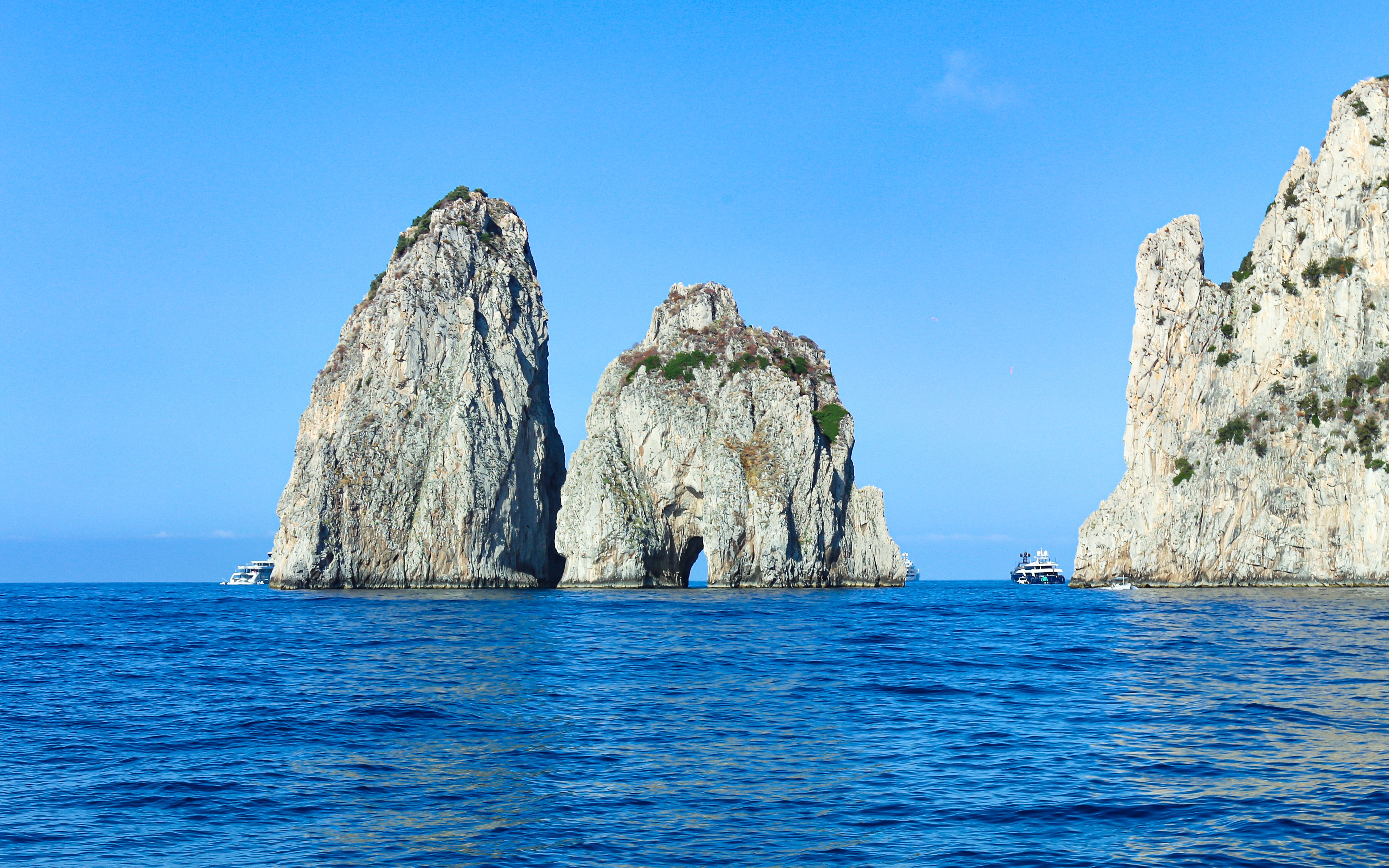 Faraglioni rock formations in blue sea off Capri, Italy, with boats nearby.