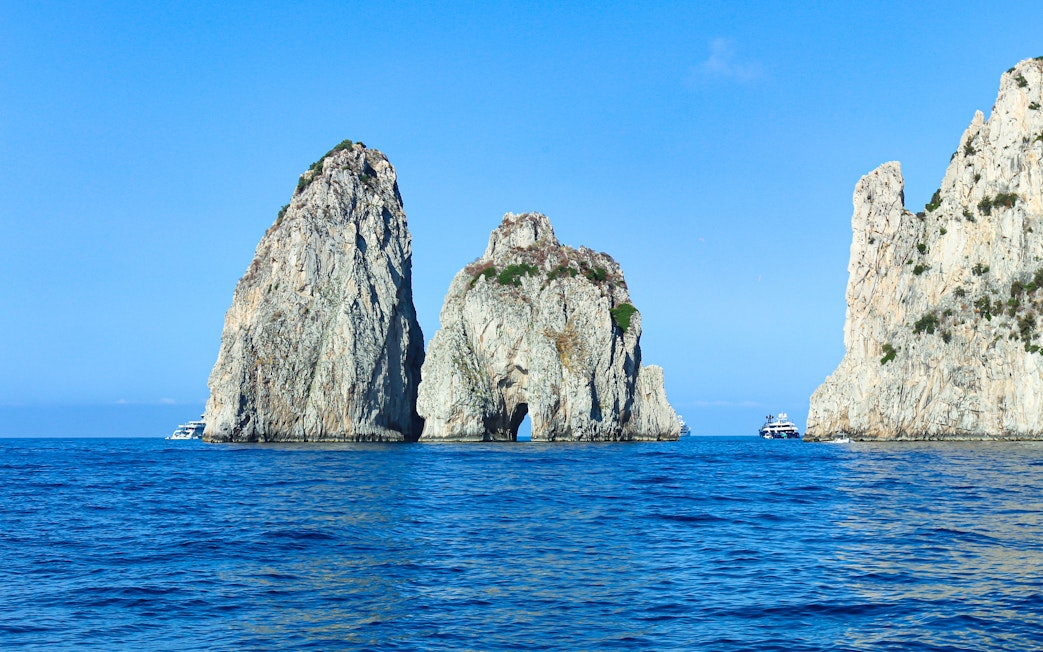Faraglioni rock formations in blue sea off Capri, Italy, with boats nearby.
