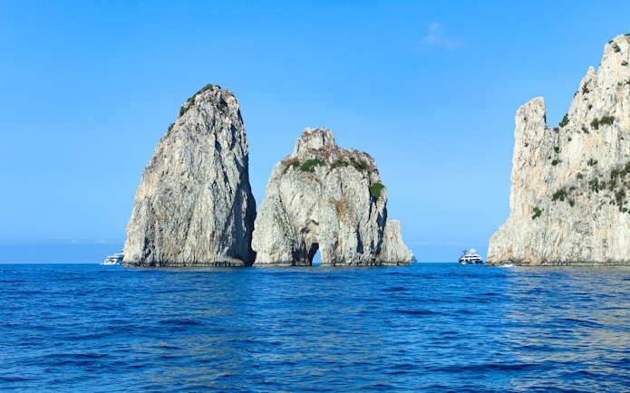 Faraglioni rock formations in blue sea off Capri, Italy, with boats nearby.