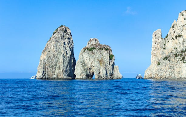 Faraglioni rock formations in blue sea off Capri, Italy, with boats nearby.