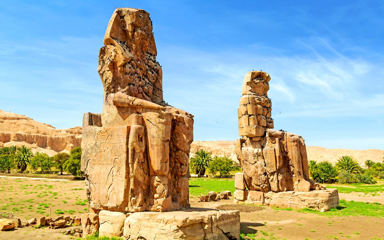 Colossi of Memnon statues in Luxor, Egypt, with desert landscape in the background.