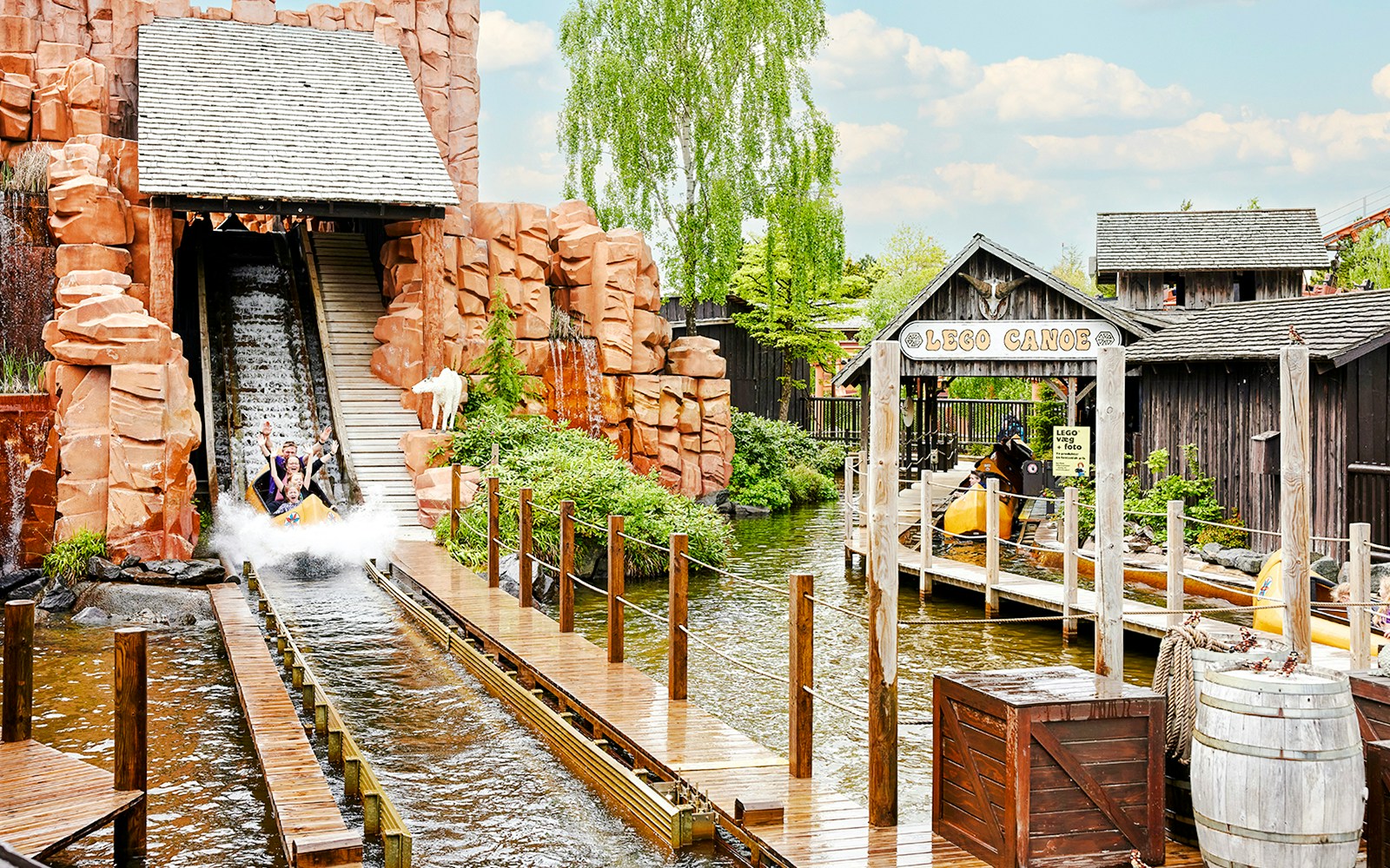 Visitors on a water slide at LEGOLAND Billund, surrounded by themed structures and greenery.
