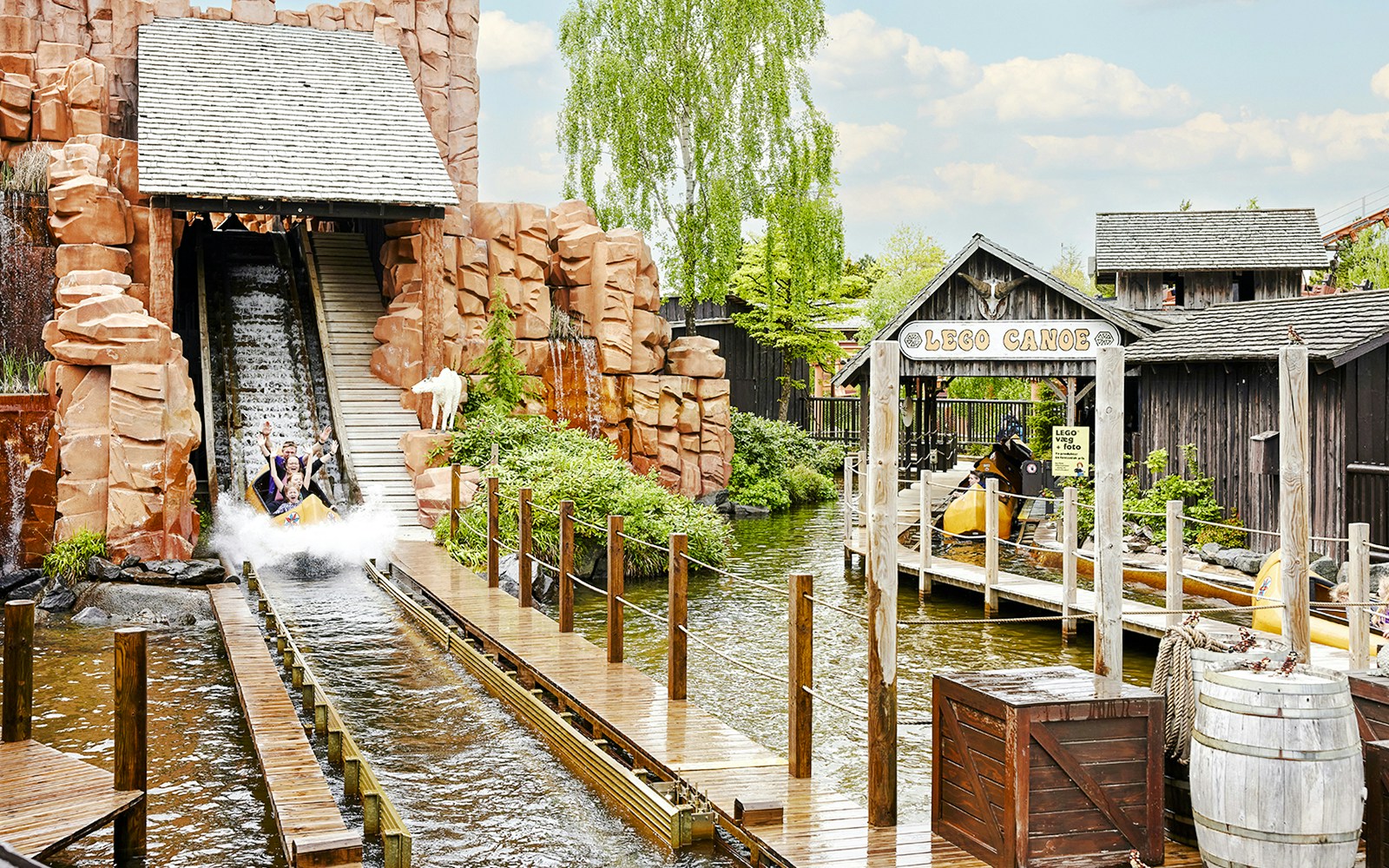 Visitors on a water slide at LEGOLAND Billund, surrounded by themed structures and greenery.