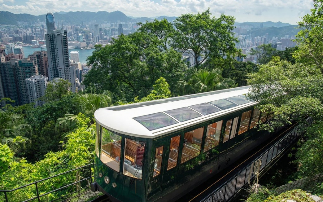 Peak Tram ascending through lush greenery with Hong Kong skyline in the background.