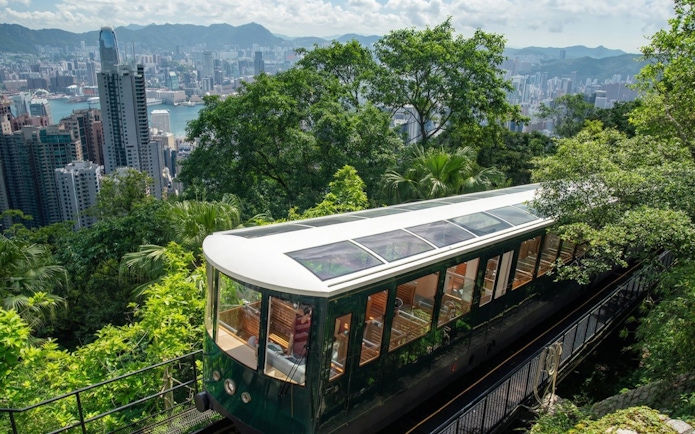 Peak Tram ascending through lush greenery with Hong Kong skyline in the background.