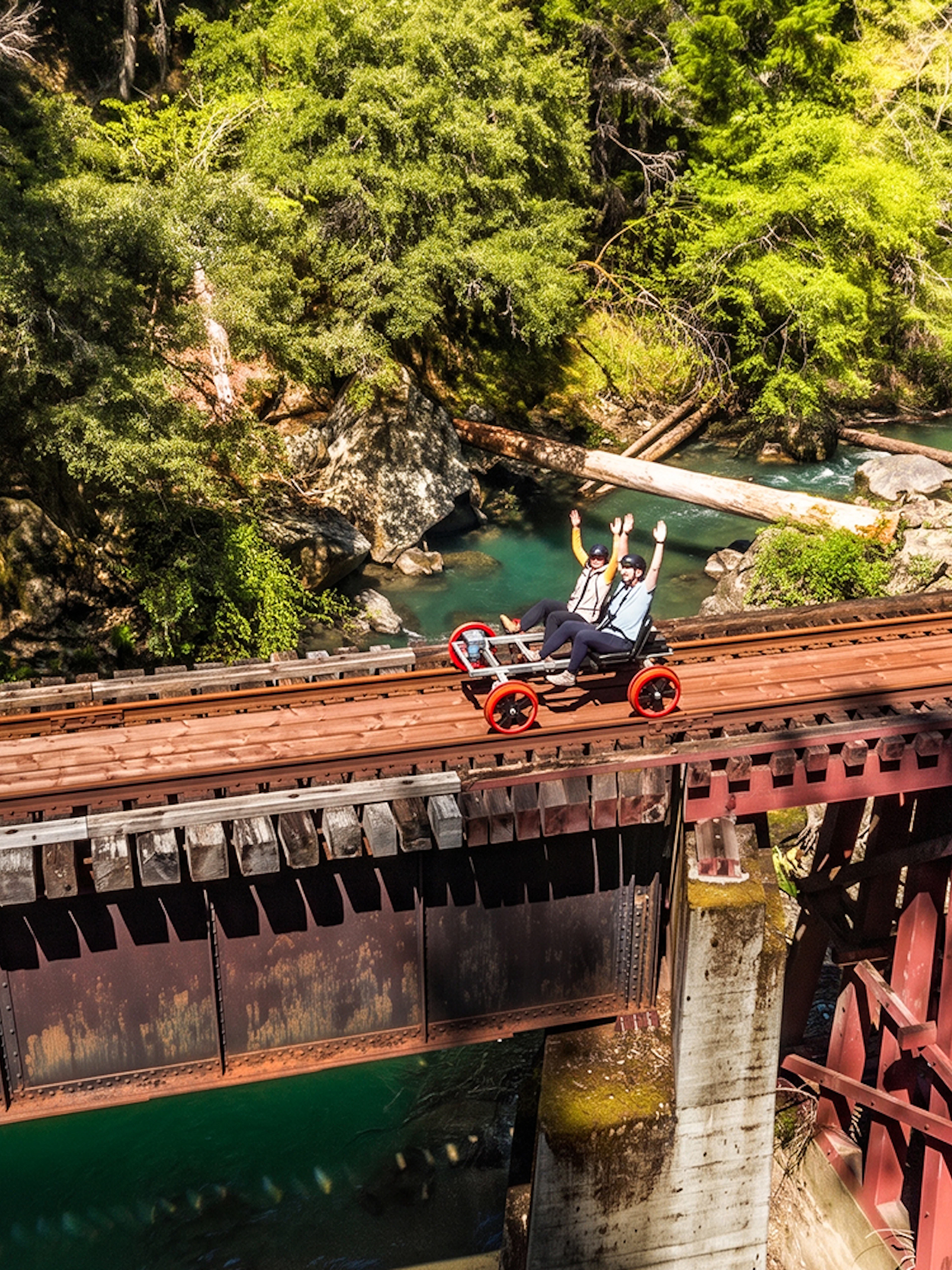 Guests riding rail bikes on a bridge over a forested river in Noyo, San Francisco.