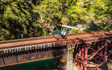 Guests riding rail bikes on a bridge over a forested river in Noyo, San Francisco.