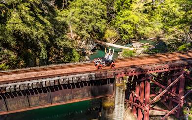 Guests riding rail bikes on a bridge over a forested river in Noyo, San Francisco.