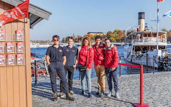 Stockholm boat tour crew standing by the waterfront with a historic ship in the background.