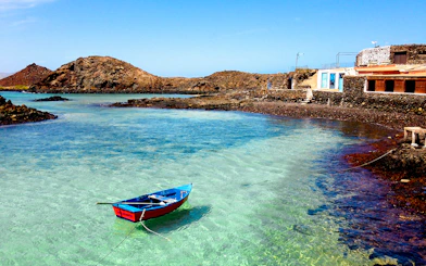Boat on clear waters near rocky shore and house, Lobos Island beach.