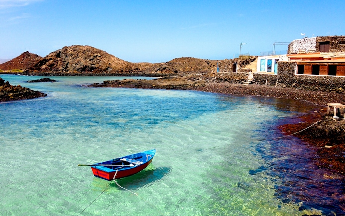 Boat on clear waters near rocky shore and house, Lobos Island beach.