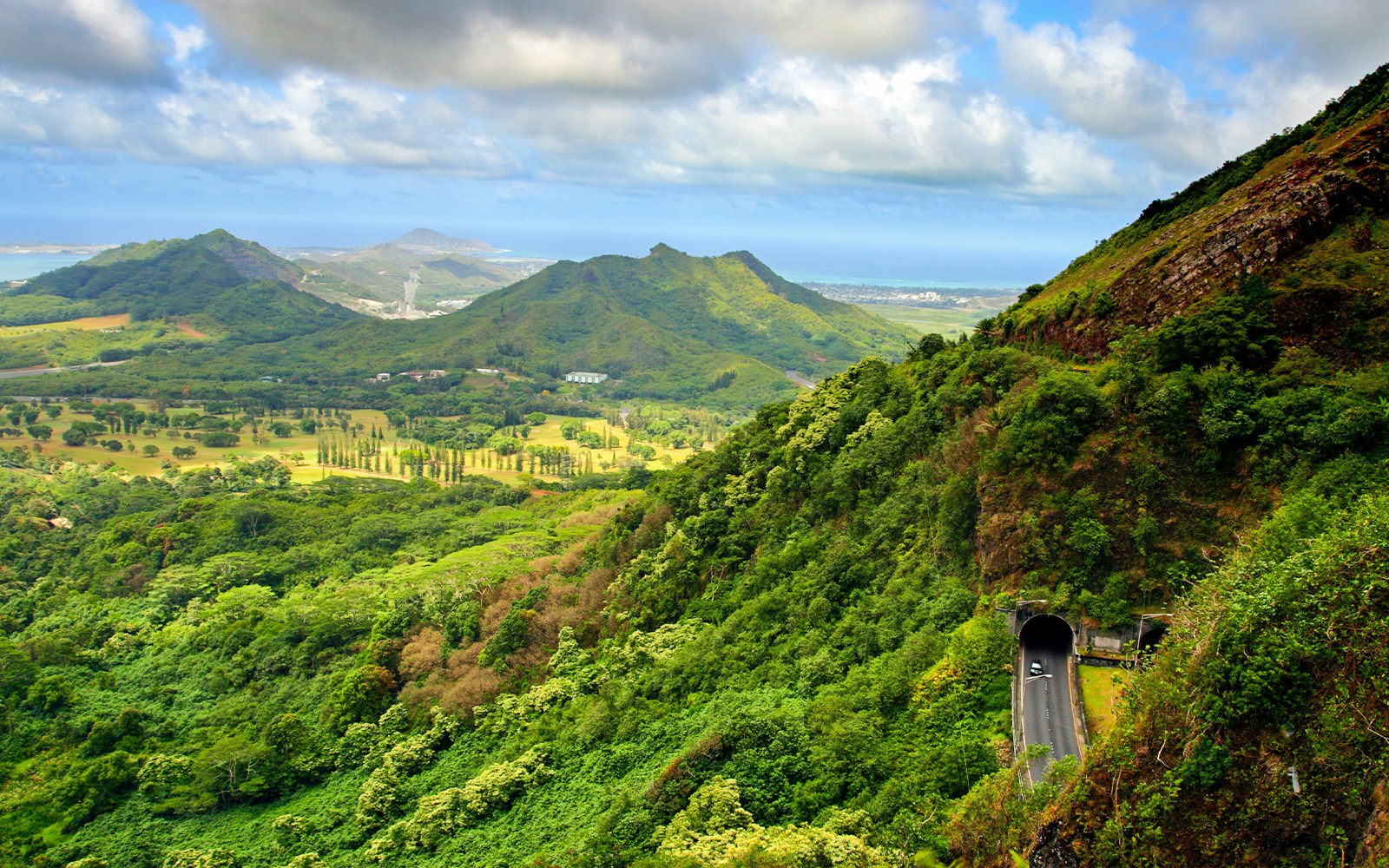 Nuuanu Pali State Park view with lush green mountains and a scenic road tunnel, O'ahu, Hawaii.