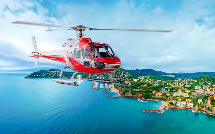 Helicopter flying over coastal town with ocean and hills in view.