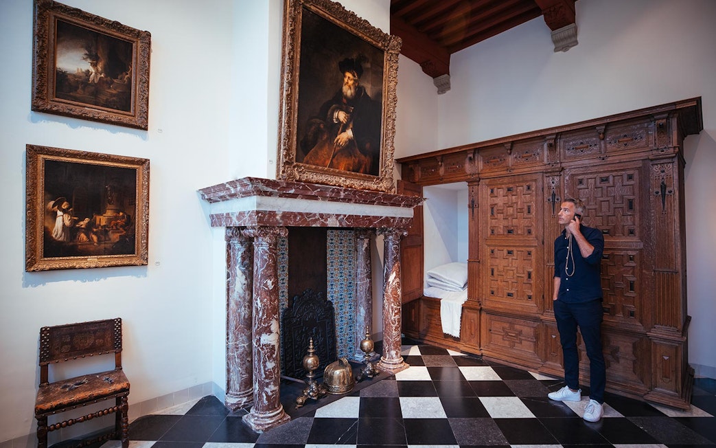 Guest exploring Rembrandt House Museum with multimedia guide, viewing historic paintings and fireplace.