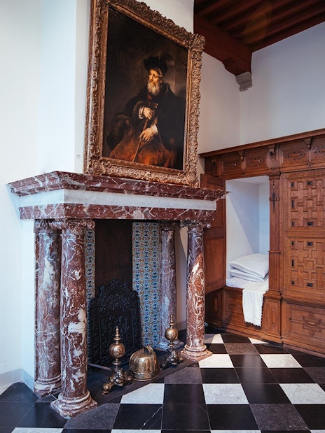 Guest exploring Rembrandt House Museum with multimedia guide, viewing historic paintings and fireplace.