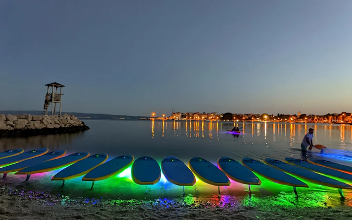 SUP boards with colorful lights on the shore at dusk during a Glow Tour in Split.