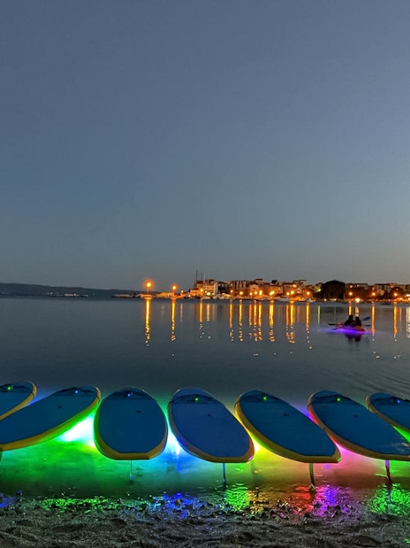 SUP boards with colorful lights on the shore at dusk during a Glow Tour in Split.