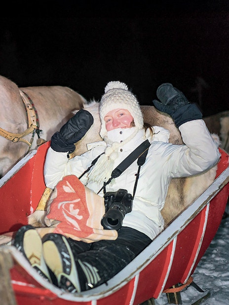 Person in sleigh with reindeer during night ride in snowy Rovaniemi forest.