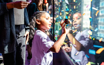 Child interacting with confetti display at One Times Square, New York City.