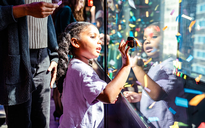 Child interacting with confetti display at One Times Square, New York City.