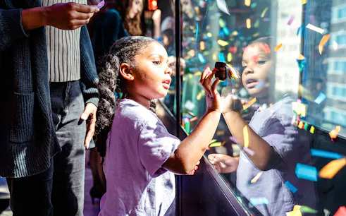 Child interacting with confetti display at One Times Square, New York City.