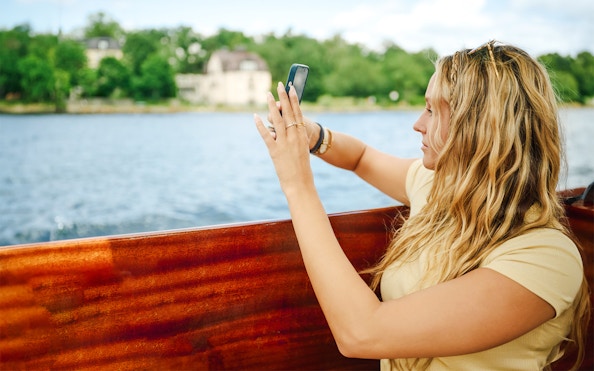 Woman taking photo on wooden boat in Stockholm Archipelago.