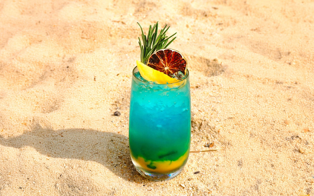 Tropical cocktail with citrus and herbs on sandy beach.