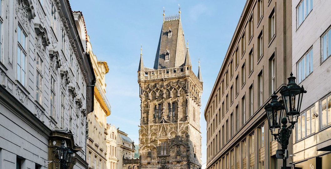 Powder Tower in Prague between historic buildings under a clear sky.
