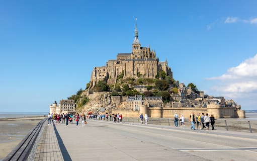 Visitors walking towards Mont Saint-Michel Abbey on a sunny day in Normandy, France.