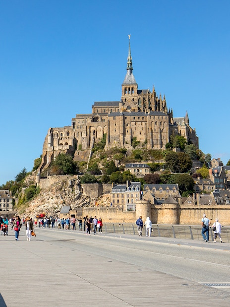 Visitors walking towards Mont Saint-Michel Abbey on a sunny day in Normandy, France.