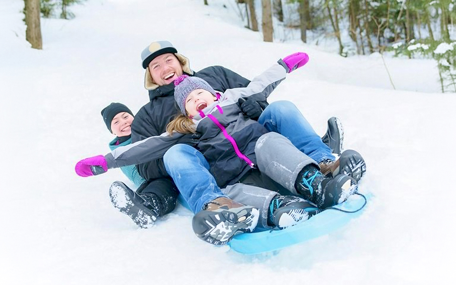 Family enjoying snow sledding in Nagano forest during snowshoeing tour.