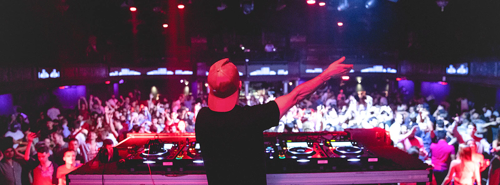 DJ performing at nightclub, view from behind with crowd dancing.