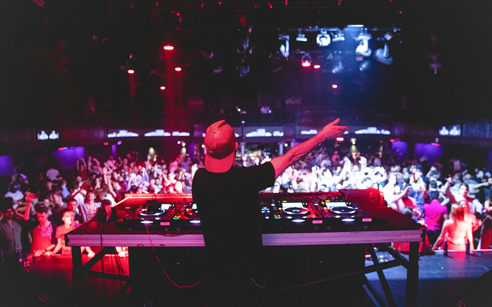 DJ performing at Ibiza nightclub, view from behind with crowd and vibrant lights.