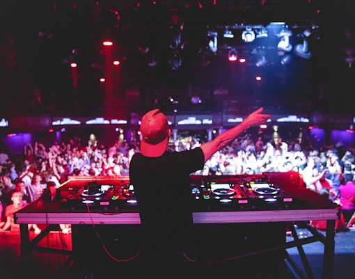 DJ performing at nightclub, view from behind with crowd dancing.