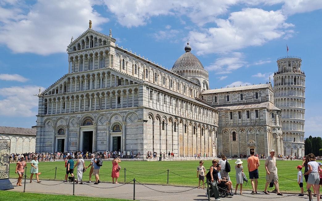 Guided tour group at Pisa's Field of Miracles with Leaning Tower in background.