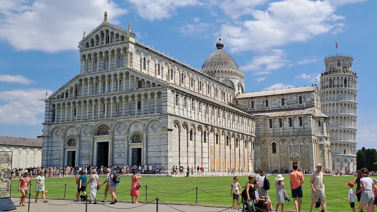 Guided tour group at Pisa's Field of Miracles with Leaning Tower in background.