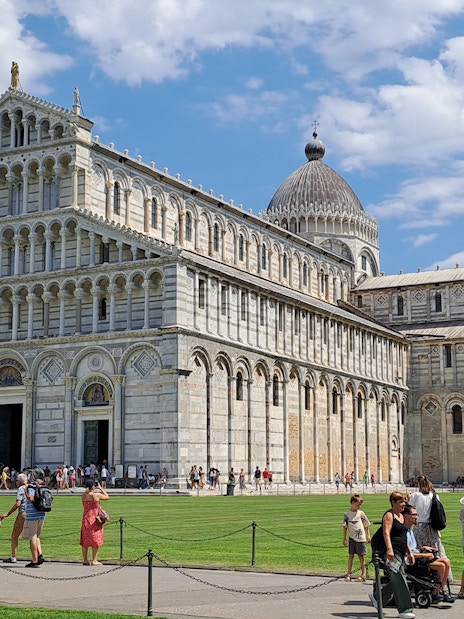 Guided tour group at Pisa's Field of Miracles with Leaning Tower in background.