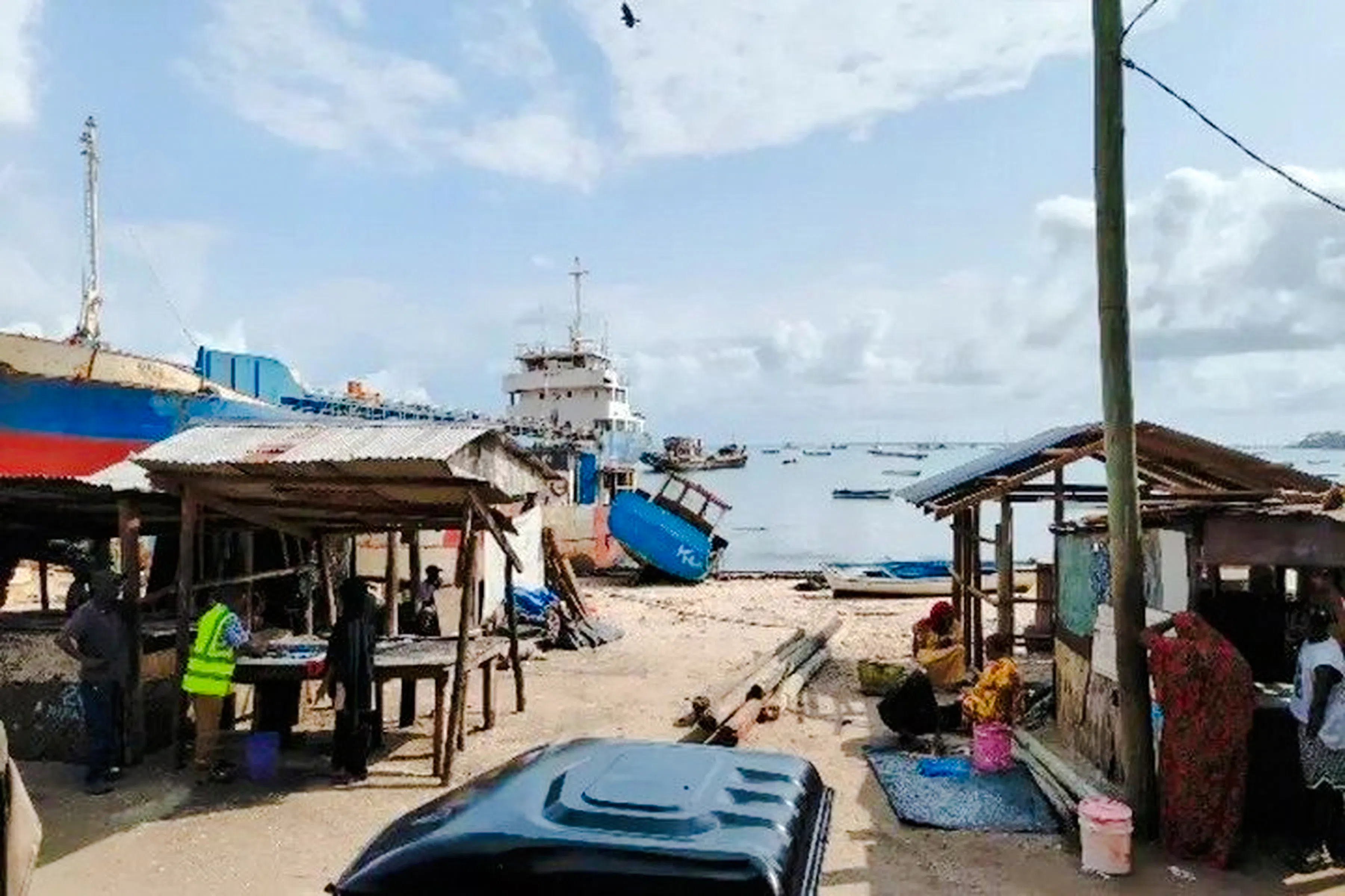 Tuk-tuk parked near fish market stalls by the shore in Dar es Salaam, Tanzania.