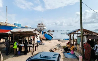 Tuk-tuk parked near fish market stalls by the shore in Dar es Salaam, Tanzania.